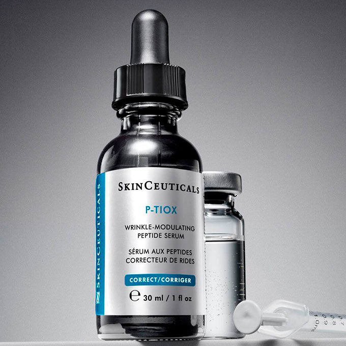 Eine Tropfflasche mit SkinCeuticals P-Tiox Serum, ein klares Flaschchen und eine kleine Spritze sind auf einem neutralgrauen Hintergrund arrangiert.