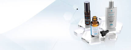 Drei Hautpflegeprodukte auf einem transparenten Regal: zwei Flaschchen mit Serum und ein Pumpspender.