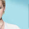 A blonde woman with short hair and a sleek hairstyle poses confidently beside a skincare product in a blue-themed promotional image.