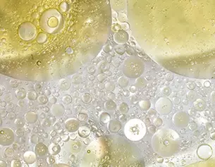 Nahaufnahme von Wasser- und Oltropfchen, die in verschiedenen Großen und Formen auf einer transparenten Oberflache schweben.