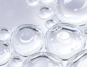 Close-up of clear water droplets, showcasing their spherical shape and reflections on a smooth surface.