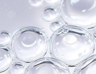 Close-up of clear water droplets, showcasing their spherical shape and reflections on a smooth surface.
