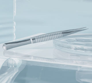 A close-up of a dental tool, specifically a tweezer, resting on a transparent surface, with soft lighting in a light blue environment.
