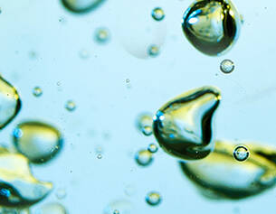 Gouttes d'eau brillantes flottant dans un liquide clair, creant des reflets et des bulles.