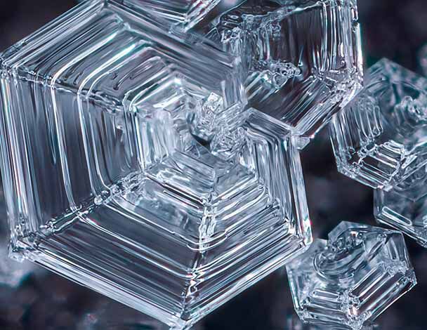 Close-up of intricate, geometric ice crystals reflecting light, showcasing their sharp edges and transparent structure.