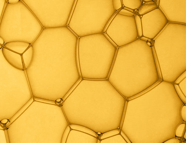 Nahaufnahme von blasenformigen Strukturen in einem goldenen Schaum, die durch Lichtreflexionen betont werden.