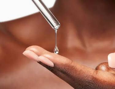 Une pipette depose une goutte de serum transparent sur le bout des doigts d’une personne.​