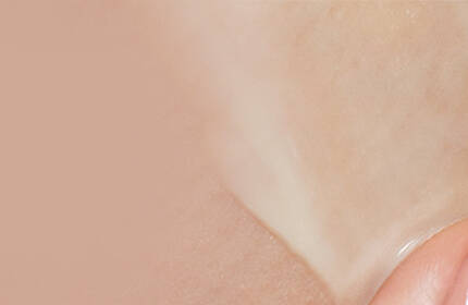 A close-up of a hand applying a smooth, creamy skincare product to the skin, with a soft, neutral background.