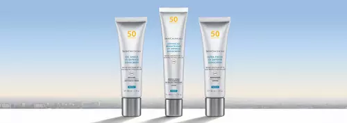 Three sleek tubes of skincare products are displayed against a soft gradient background that transitions from light blue to pale yellow, suggesting a serene skyline.