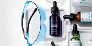 Une disposition de produits de soin de la peau, comprenant des flacons de serum, un pot de creme, des cotons-tiges et un masque, sur un fond blanc.