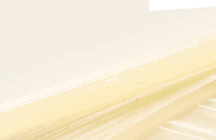 A close-up of a smooth, creamy texture with light yellow tones, set against a pale background, showcasing layers and ridges.