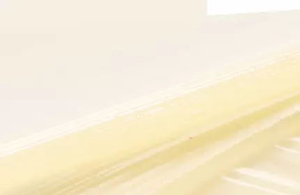 A close-up of a smooth, creamy texture with light yellow tones, set against a pale background, showcasing layers and ridges.
