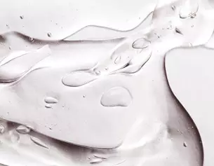 Close-up of a translucent gel with droplets, creating a smooth, flowing texture on a light background.