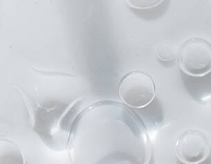 Gouttes d'eau transparentes sur une surface blanche, creant un effet de lumiere et de reflexion.