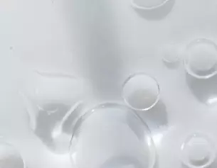 Gouttes d'eau transparentes sur une surface blanche, creant un effet de lumiere et de reflexion.