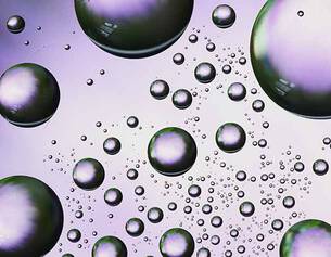 Close-up of iridescent water droplets floating on a textured surface, reflecting light in shades of green and purple.