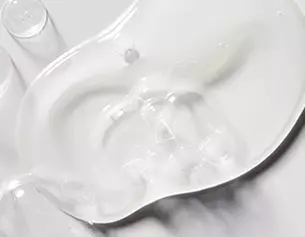 Un gel transparent glissant sur une surface blanche, creant des formes fluides et irregulieres.