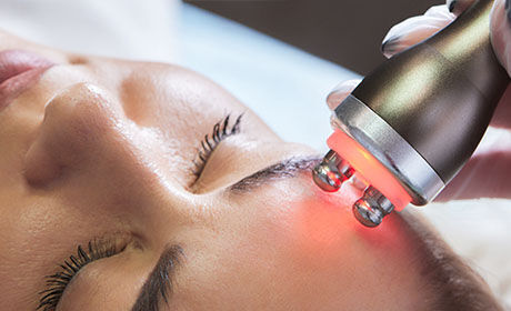 Gros plan d’un soin du visage avec un appareil a lumiere rouge sur la peau.