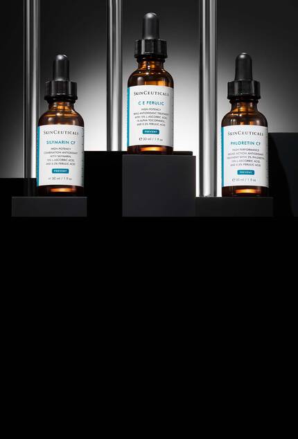 Trois flacons de serums antioxydants SkinCeuticals : Silymarin CF, C E Ferulic et Phloretin CF, disposes sur des socles noirs a plusieurs niveaux, sur un fond sombre rehausse de touches metalliques verticales.