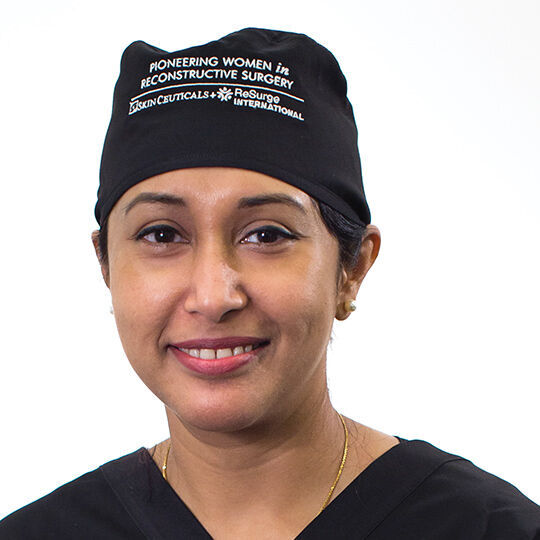 Une femme souriante portant une blouse de medecin et un bonnet noir.