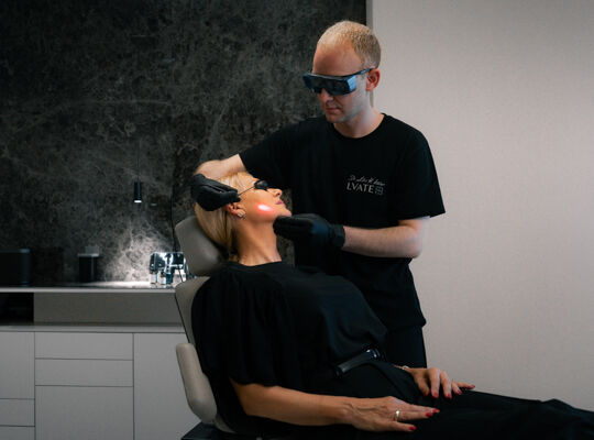 Un medecin portant une tenue de protection et des lunettes de securite realise un traitement au laser sur une patiente allongee.​