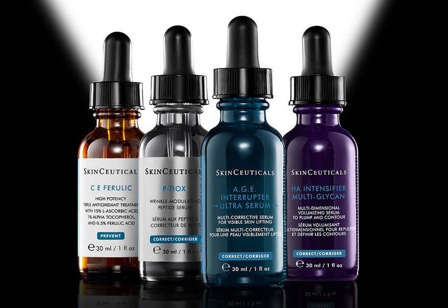 Quatre serums SkinCeuticals – C E Ferulic, H.A. Intensifier, A.G.E. Interrupter Ultra Serum et Phyto Corrective – sur un fond sombre, entoures d’un halo de lumiere.