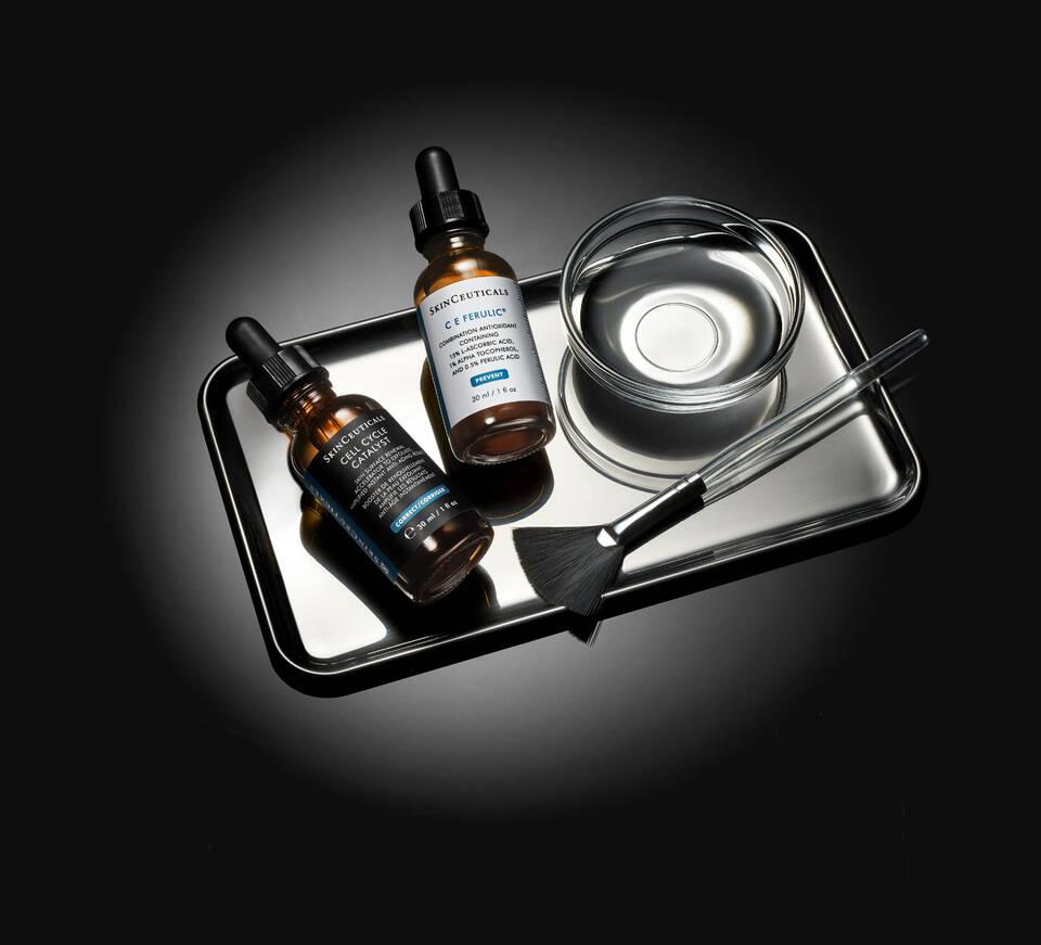 Quatre flacons de serums pour la peau sur une etagere, avec un fond noir elegant.