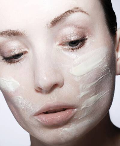 Femme au visage partiellement recouvert d'une creme de soin, regard pensif.