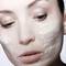 Femme au visage partiellement recouvert d'une creme de soin, regard pensif.