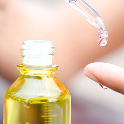 Bouteille d'huile avec un compte-gouttes, une goutte s'apprete a tomber sur un doigt.