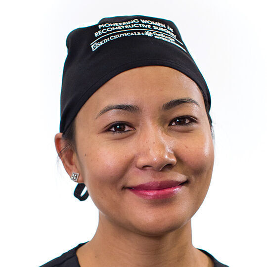 Une professionnelle de la sante souriante portant une charlotte noire, avec un fond blanc.