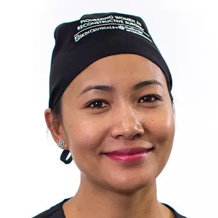 Une professionnelle de la sante souriante portant une charlotte noire, avec un fond blanc.